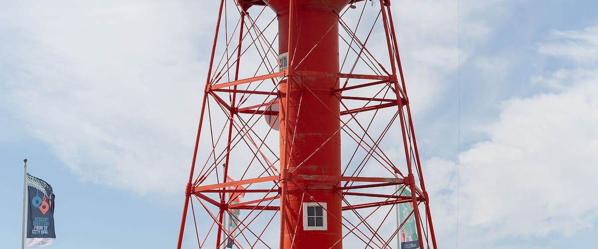 A red lighthouse with a white top, situated next to a staircase leading up to it.