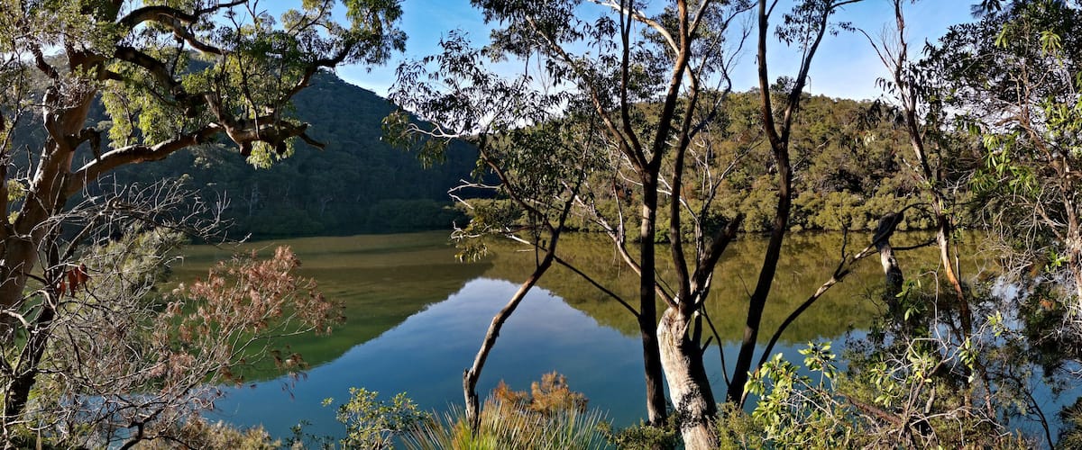 Early morning panoramic view of a calm creek with beautiful reflections of blue sky, mountains and trees on water, Cowan Creek, Bobbin Head, Ku-ring-gai Chase National Park, New South Wales Australia