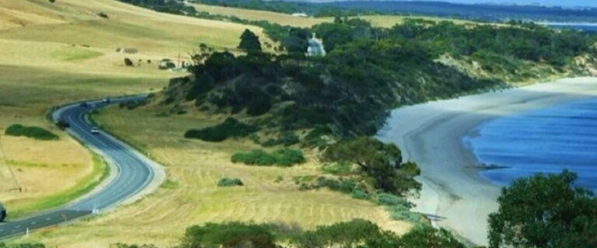 A coastal road curving through a hilly landscape with a beach on one side.