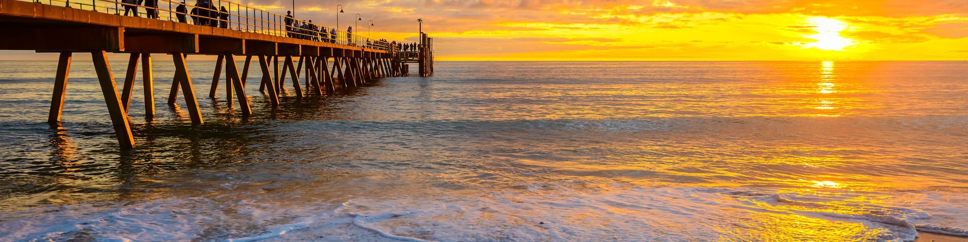 A pier extending into the ocean at sunset with waves lapping at the shore.
