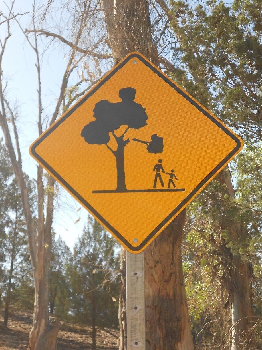 A yellow warning sign with a tree and two figures, one adult and one child, walking near it.