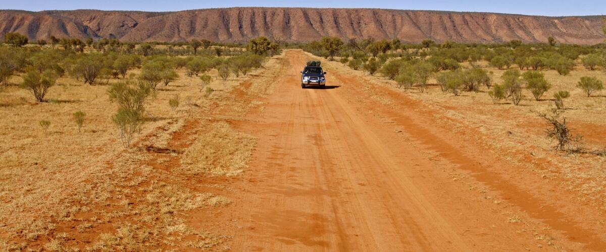 A vehicle on a dirt road in a desert landscape with sparse vegetation and a mountain range in the background.