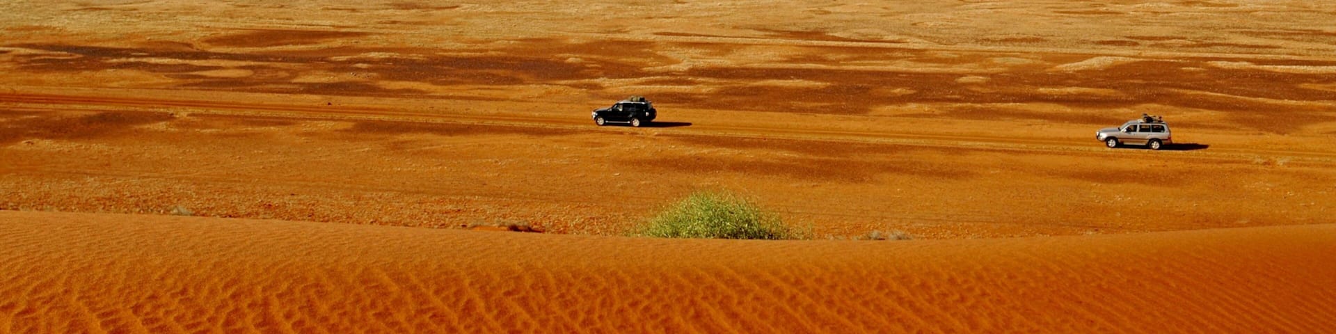 A vast desert landscape with two vehicles on the sand.