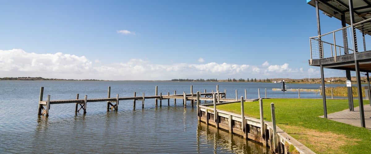 A wooden pier extending into calm water, a grassy area, and a blue-roofed structure.