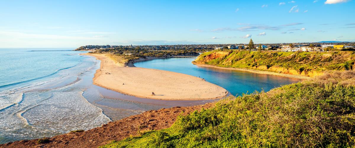 A coastal landscape with a sandy beach, a curving bay, and a distant town with buildings.