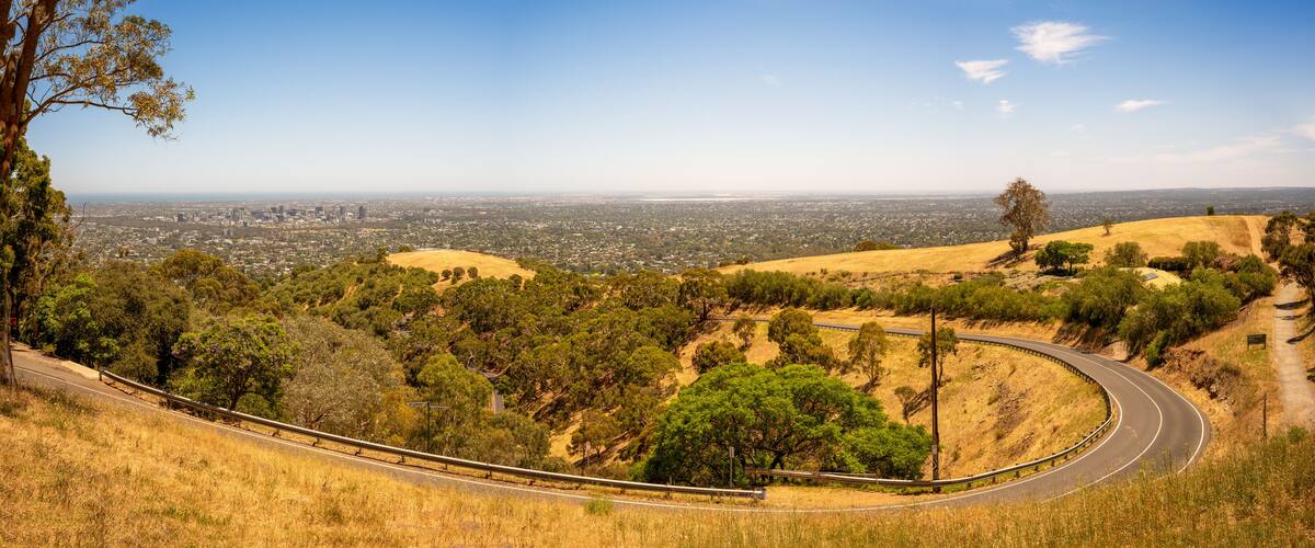A winding road through a hilly landscape with a city in the distance.