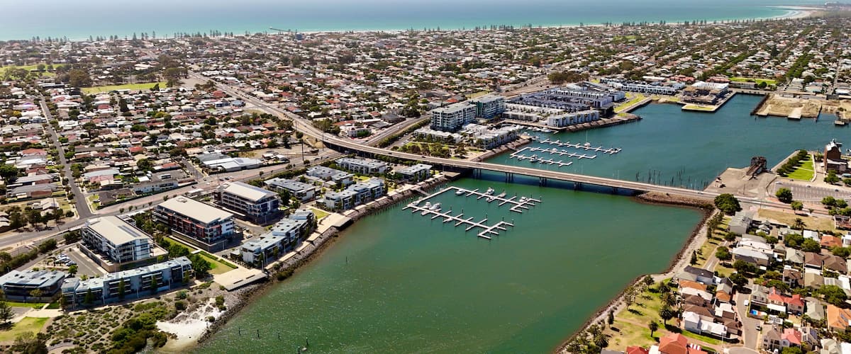 Vista aérea de una ciudad costera con un puerto deportivo, zonas residenciales y un puente que conecta diferentes partes de la ciudad.