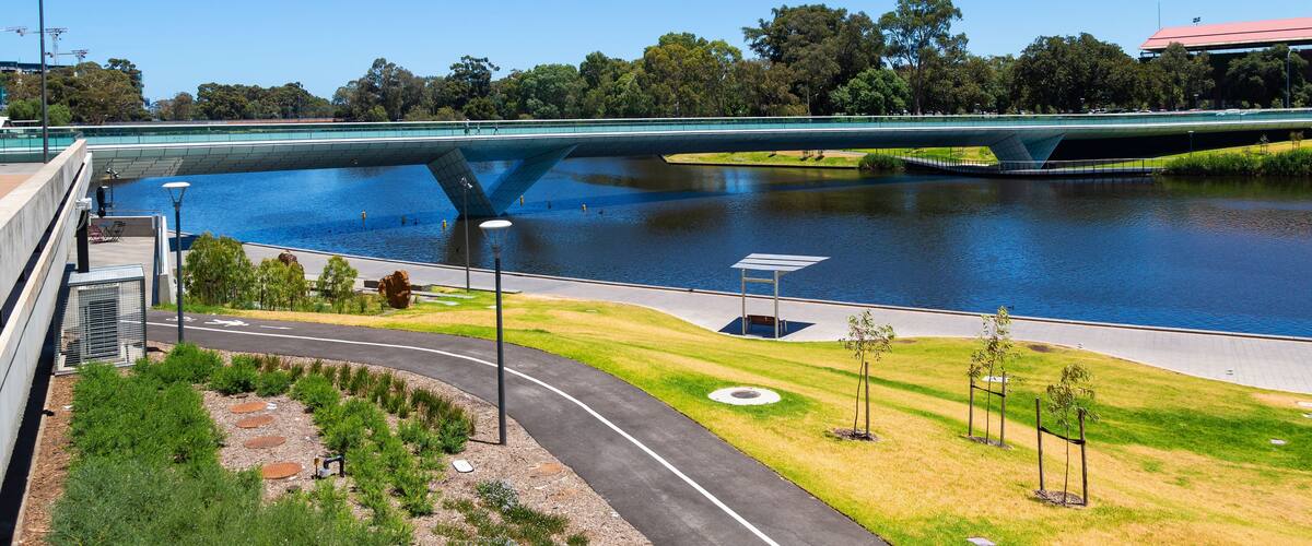 A modern bridge over a river, surrounded by greenery and a clear blue sky.