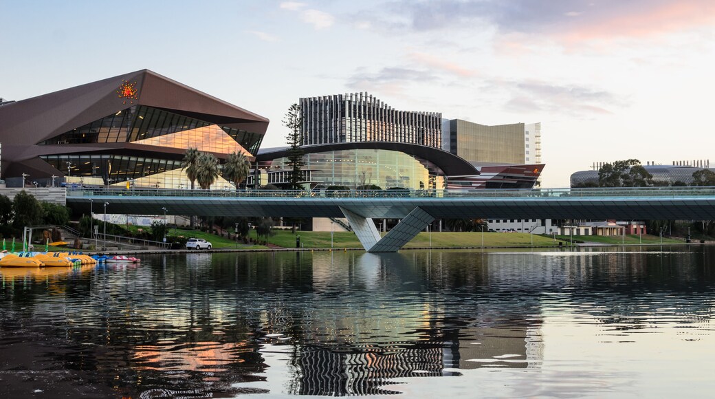 A modern bridge over a body of water with reflections, a distinctive building with a unique roof design, and another building with a patterned facade.