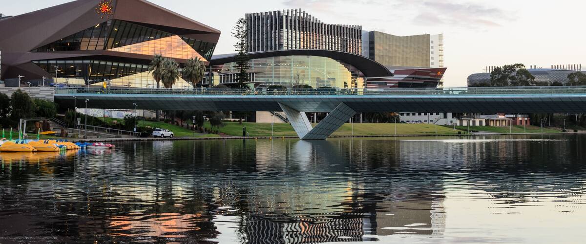 A modern bridge over a body of water with reflections, a distinctive building with a unique roof design, and another building with a patterned facade.