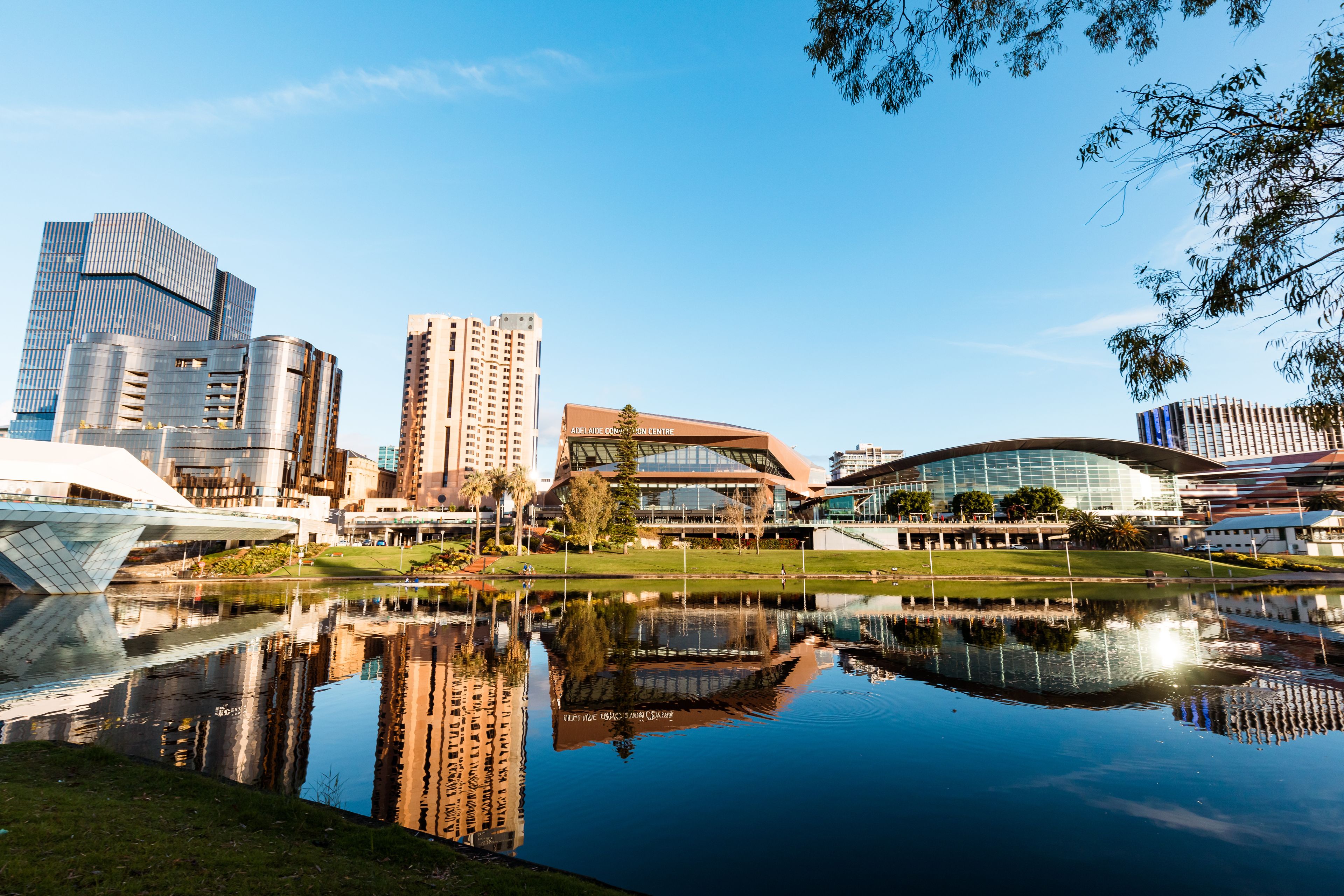A cityscape with modern architecture, a central building labeled 'Adelaide Convention Centre,' and a calm water body reflecting the buildings.