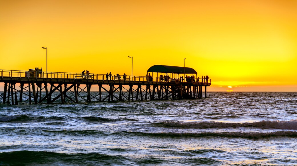 A pier extending into the ocean at sunset with people walking along it.