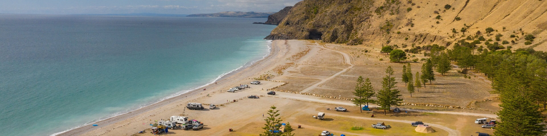 Um camping costeiro com tendas, veículos recreativos e automóveis ao longo da praia e arredores.