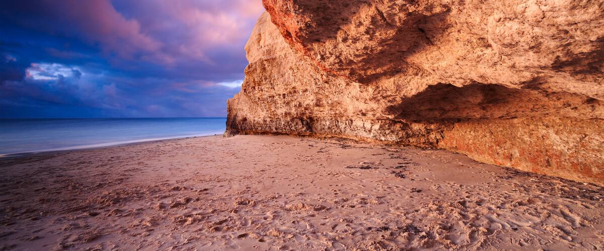 A beach with a large rock formation and a clear sky.