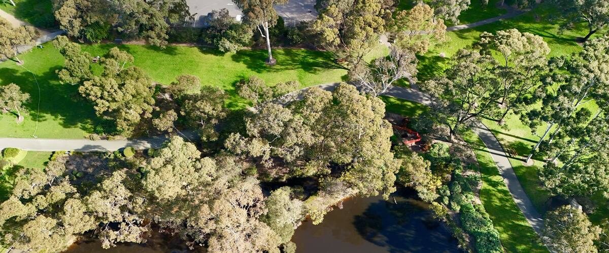 Vue aérienne d’un parc avec un lac, de nombreux arbres et un espace de stationnement.