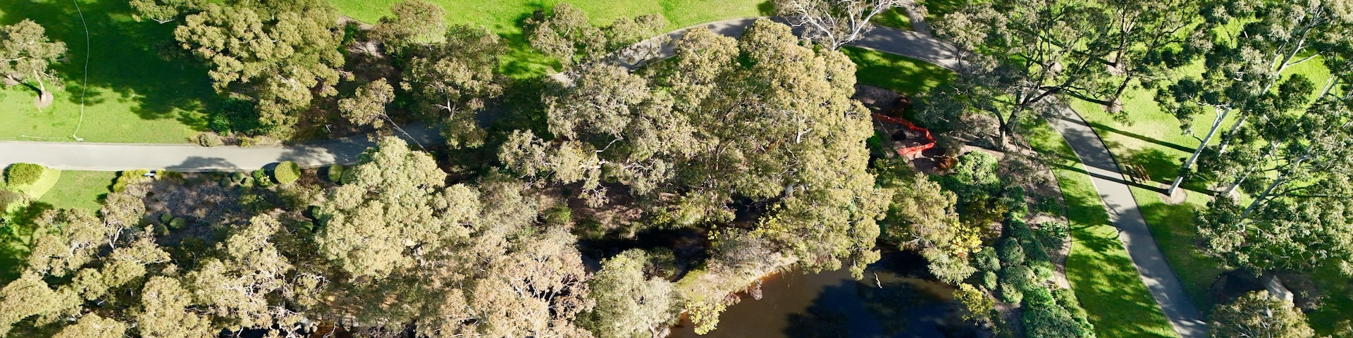 An aerial view of a park with a lake, dense trees, and a parking area.