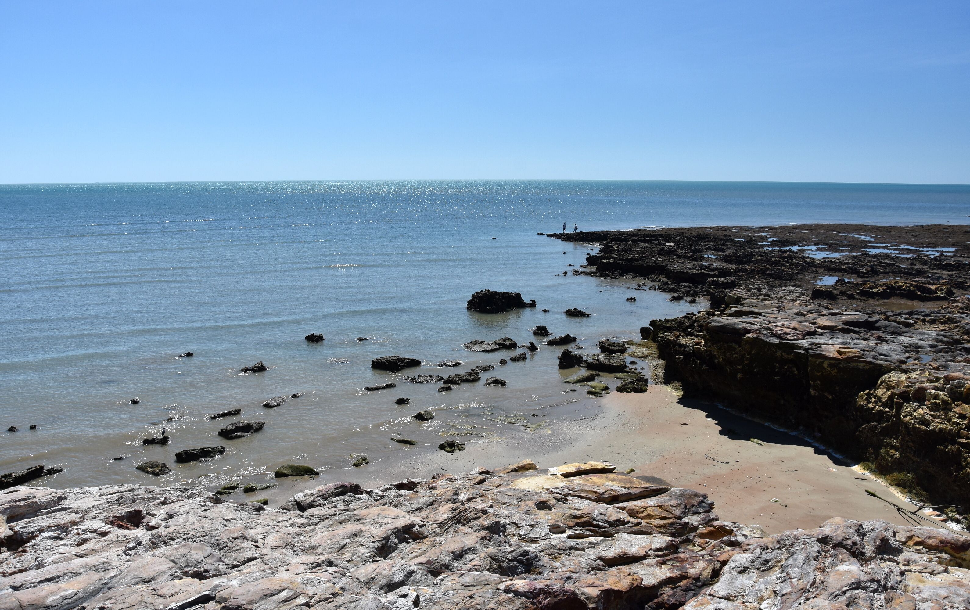 A rocky shoreline with scattered rocks in the water and a clear blue sky.