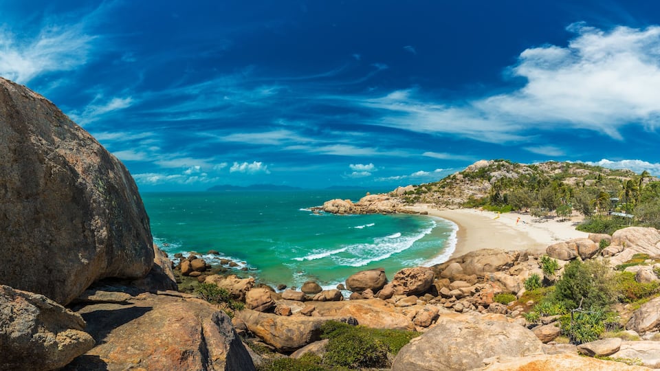 Una costa rocosa con un gran bloque de piedra, mar turquesa y una playa de arena.