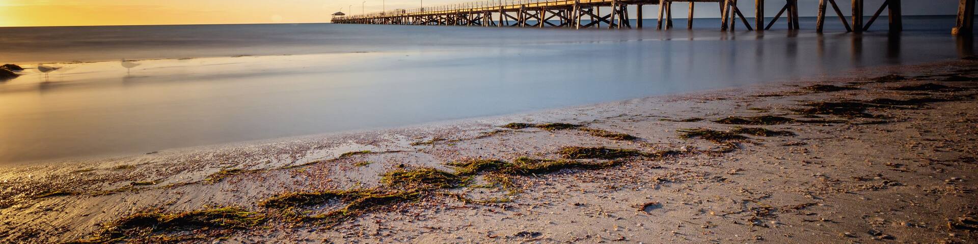A pier extending into calm waters at sunset with a clear sky.