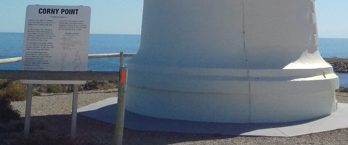 A white lighthouse with a sign reading "Corny Point" in front of a clear blue sky.