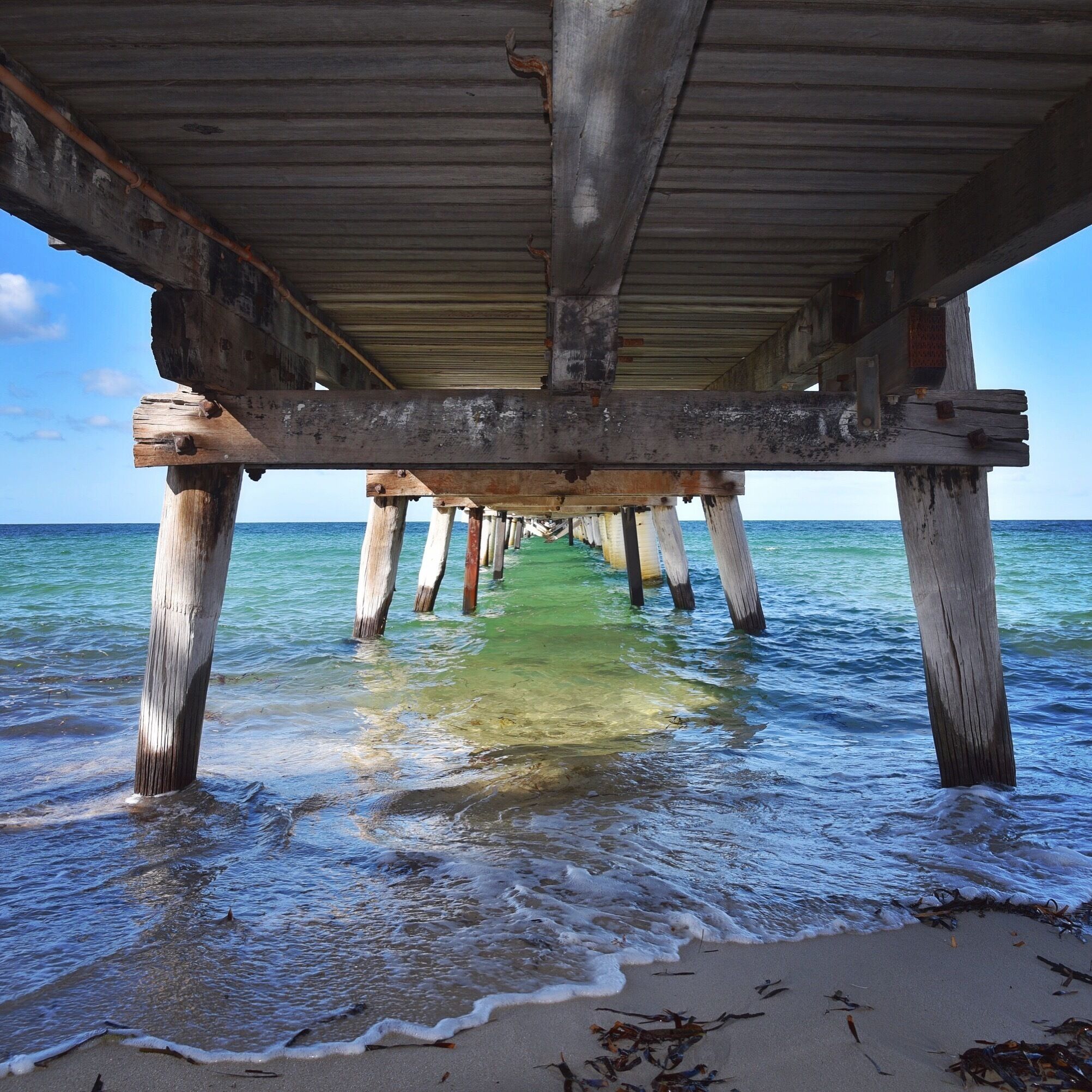 A wooden pier extending into the ocean with clear water and a sandy beach at the end.