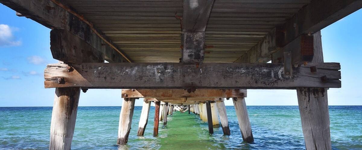 A wooden pier extending into the ocean with clear water and a sandy beach at the end.