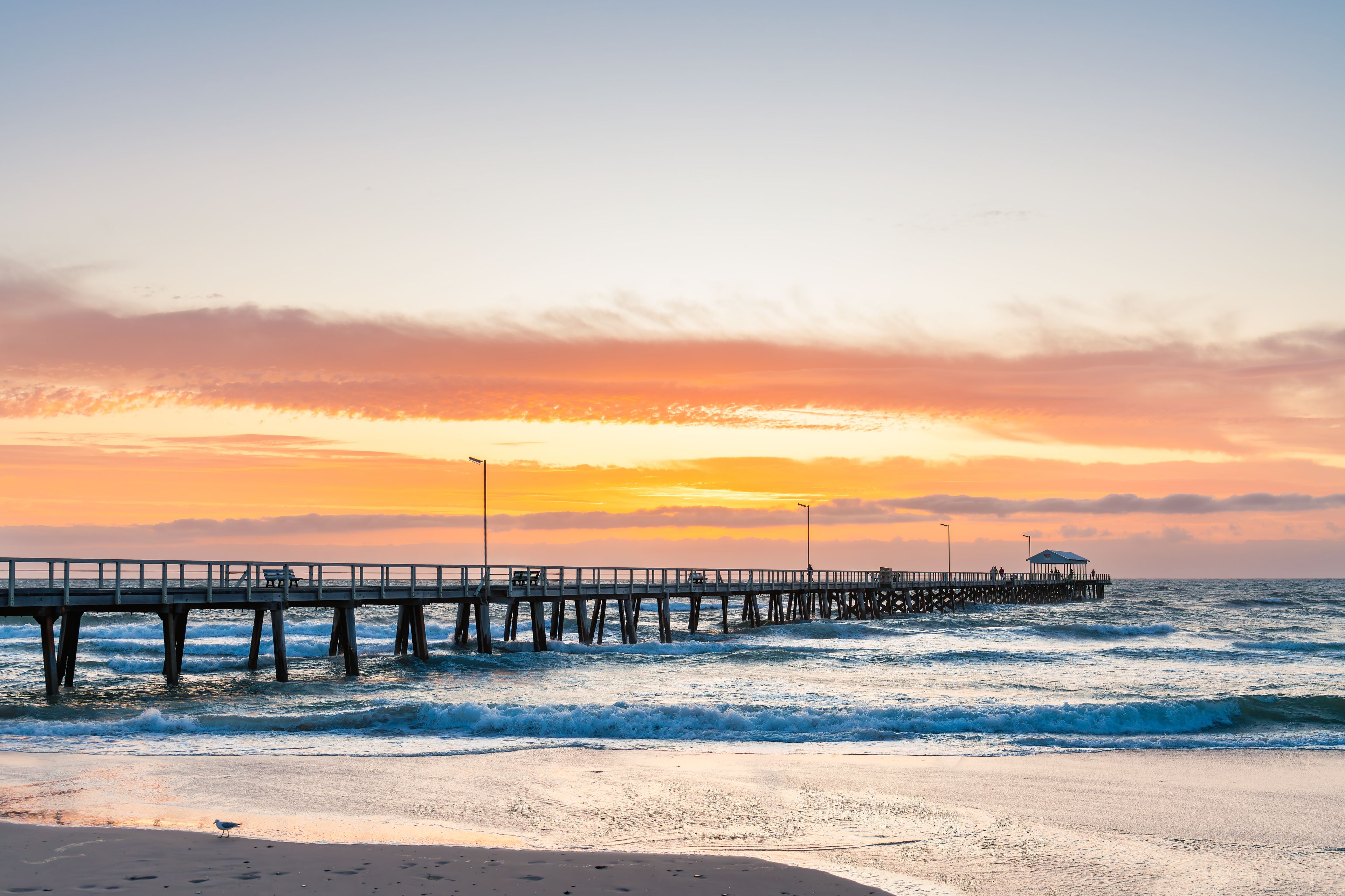 People walking along Henley Beach Jetty during a stormy dramatic sunset viewed from the shoreline in Adelaide, South Australia.