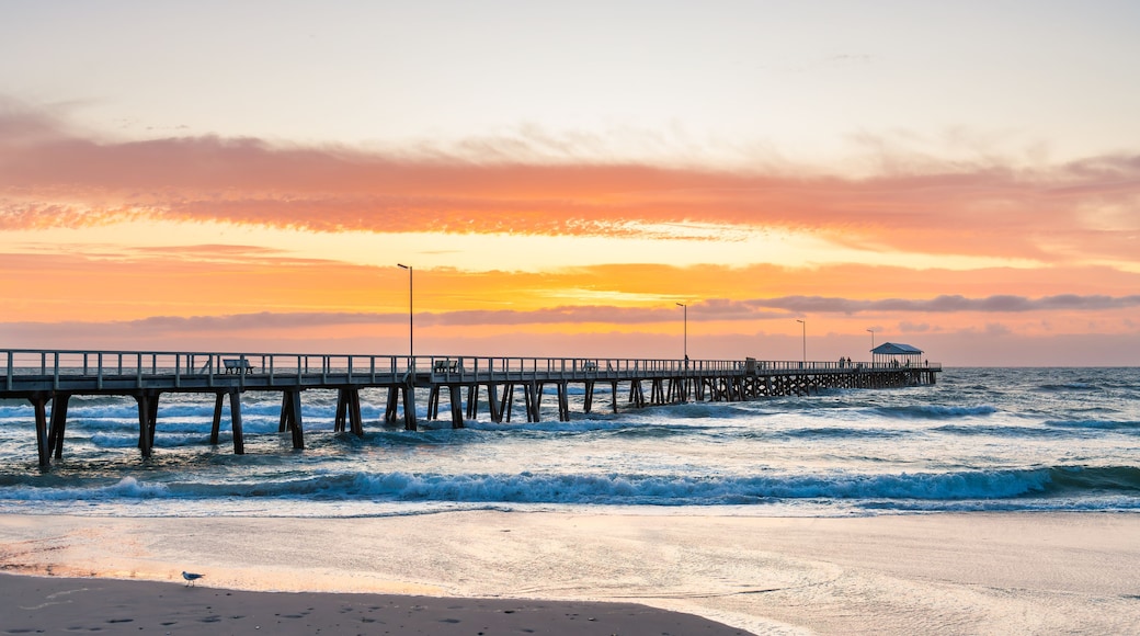 A pier extending into the ocean with waves crashing against it, a clear sky, and a sunset.