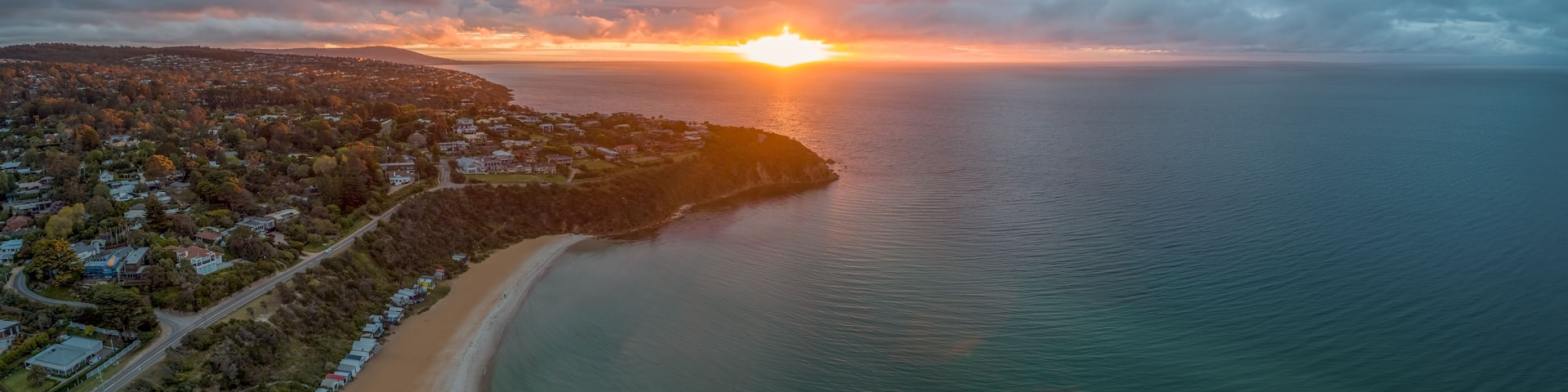 A coastal town at sunset with a beach and houses along the shoreline.