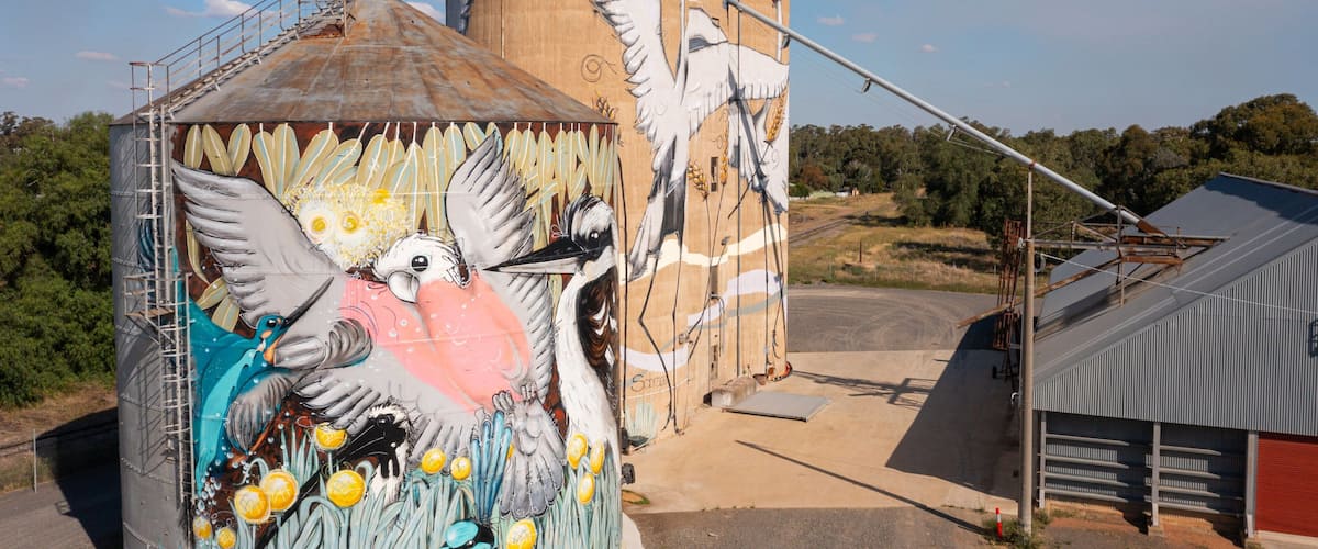 A large grain silo with a mural of birds and a silo with a metal roof.
