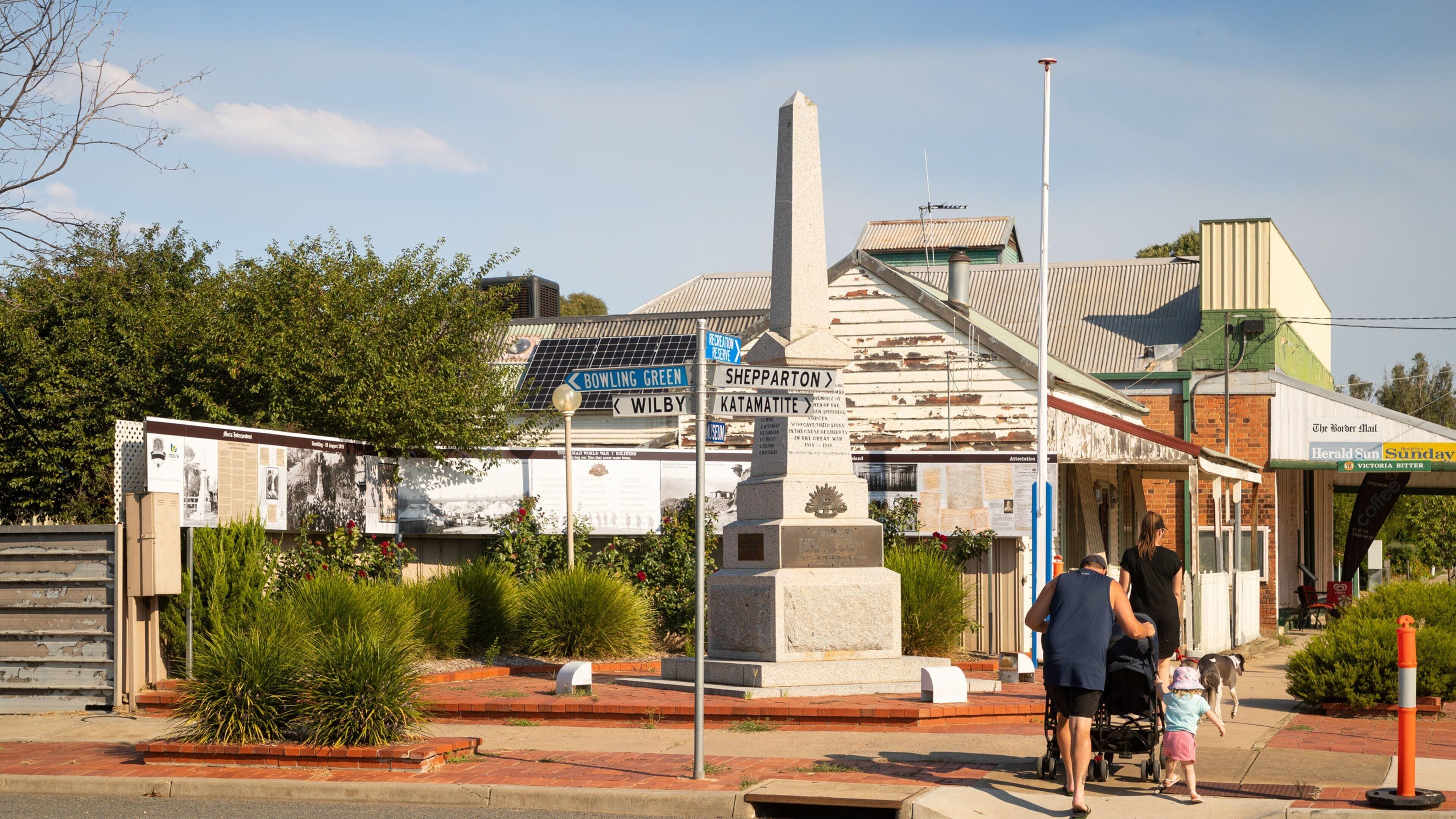 Un monumento con señales indicativas, una estatua y un edificio con señalización que indica 'Bowling Green' y 'Shepparton'.