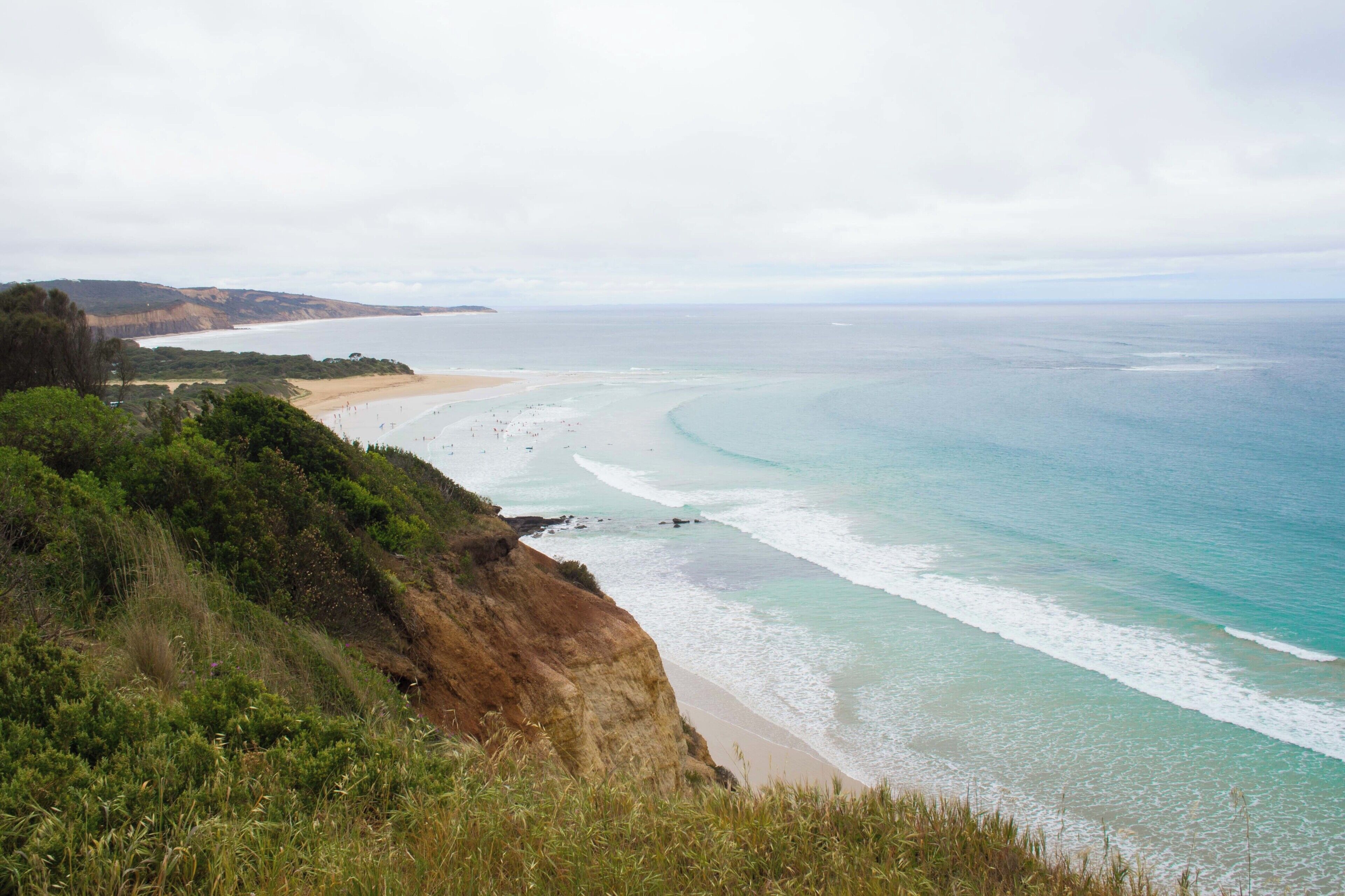 A coastal landscape with a sandy beach, clear turquoise waters, and a cliff with greenery.