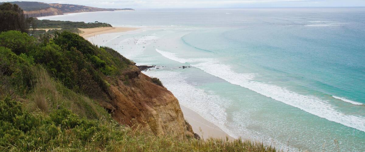A coastal landscape with a sandy beach, clear turquoise waters, and a cliff with greenery.