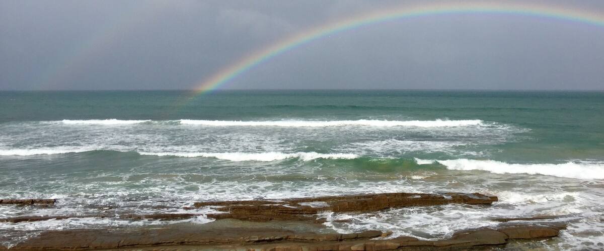 A beach with waves and a rainbow over the ocean.