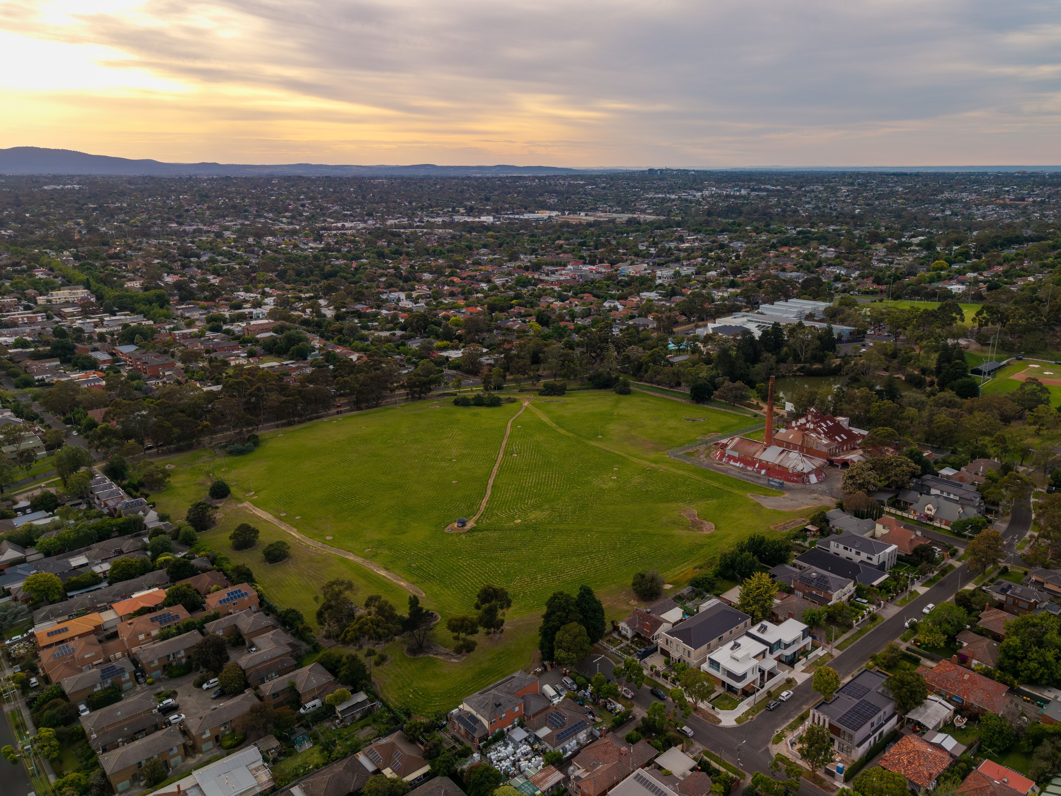 Aerial View of Box Hill Brickworks and Expansive Parkland Surrounded by Residential Suburbs Under a Warm, Cloudy Sky at Dusk