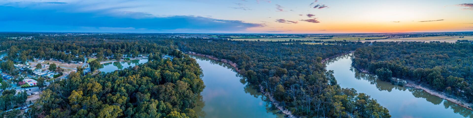 A river winding through a densely forested area with a small settlement on one side.
