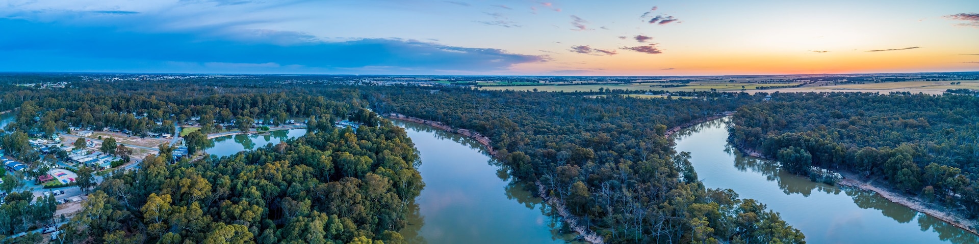 A river winding through a densely forested area with a small settlement on one side.