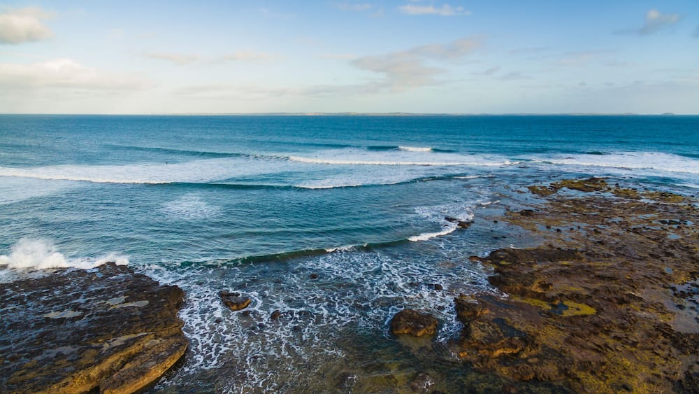 Une côte rocheuse où les vagues s’écrasent sur le rivage sous un ciel dégagé.