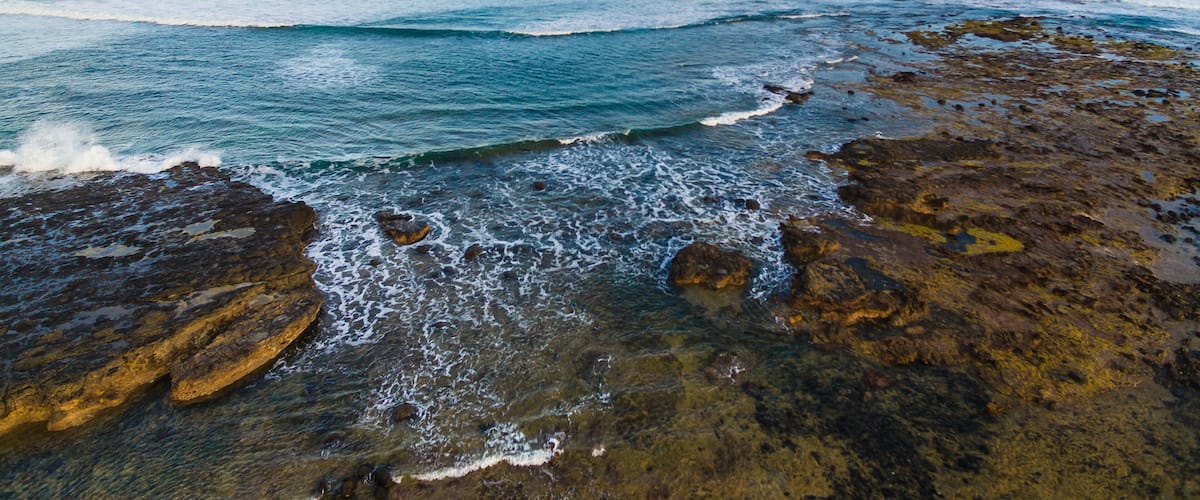 A rocky coastline with waves crashing against the shore under a clear sky.
