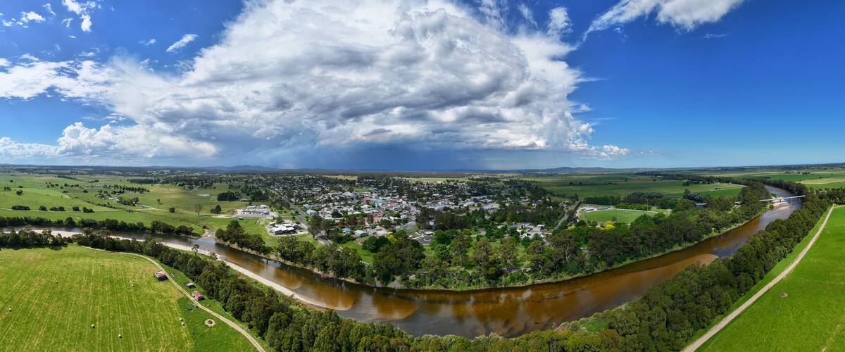 A river winding through a town surrounded by green fields and a large cloud in the sky.