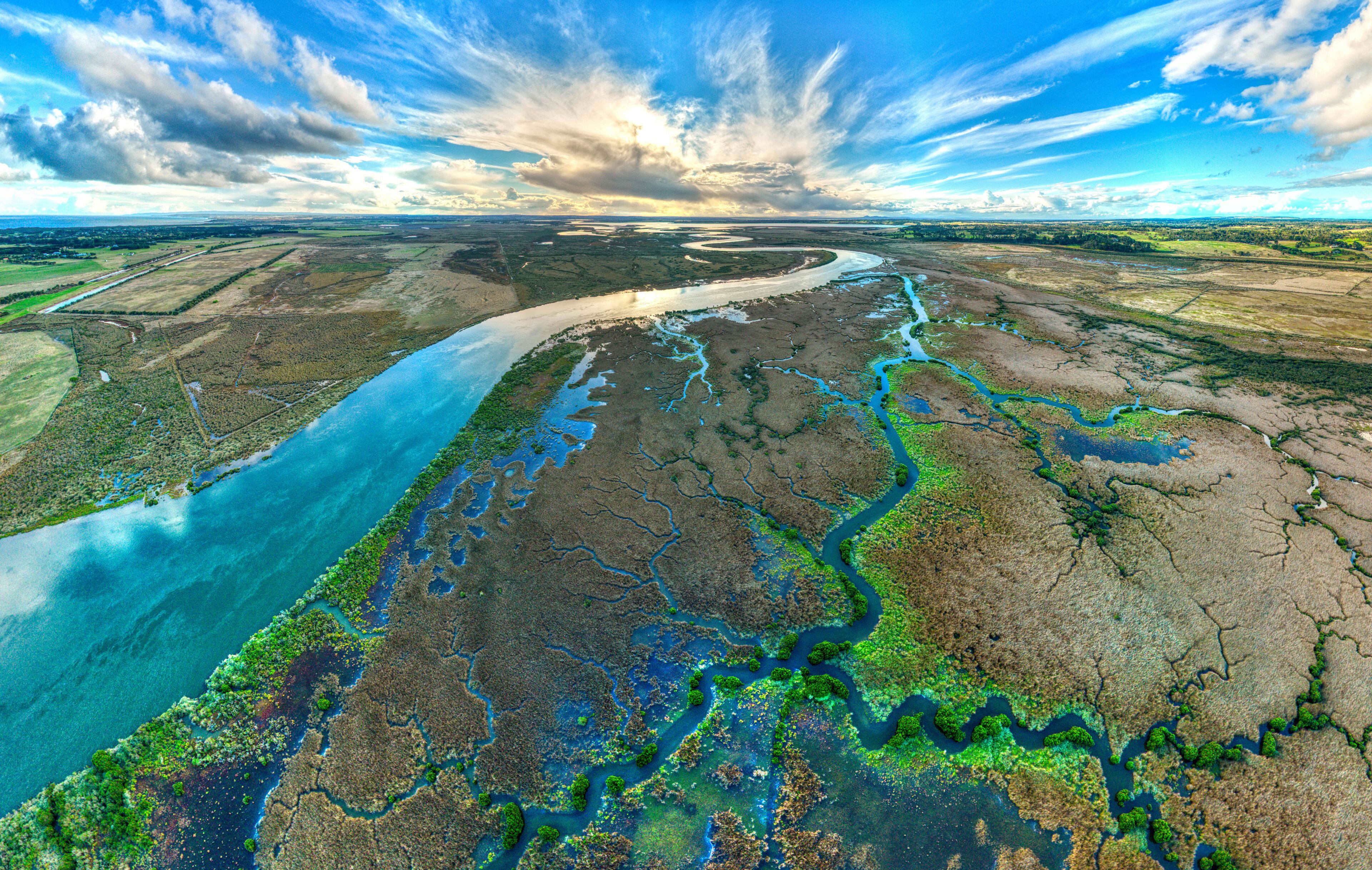 A river winding through a landscape with green vegetation and a blue sky.