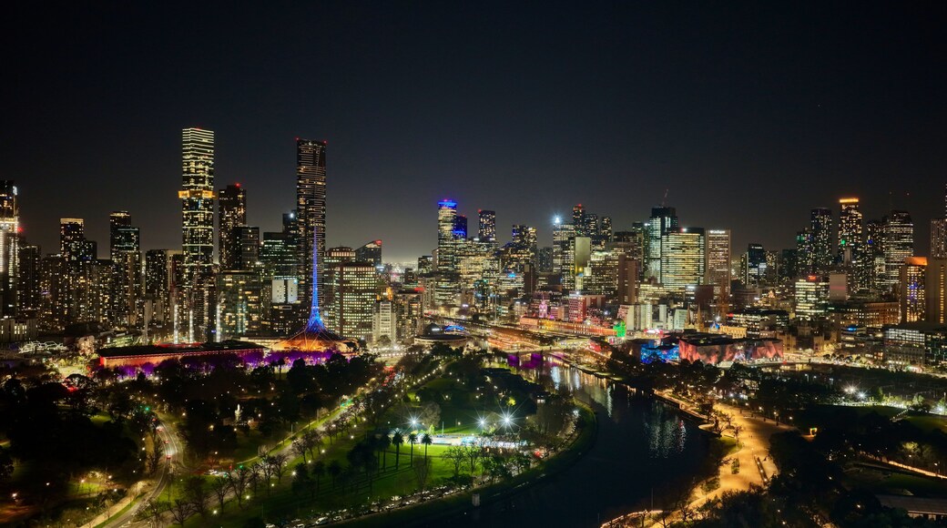A nighttime cityscape with illuminated skyscrapers and a river reflecting the lights.