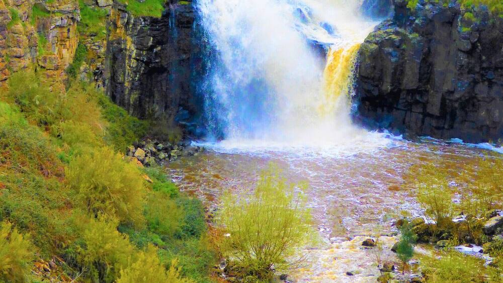 Ein Wasserfall stürzt über steinige Klippen, umgeben von üppigem Grün.