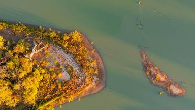 An aerial view of a coastal area with a sandy beach, a small island, and a boat creating ripples in the water.