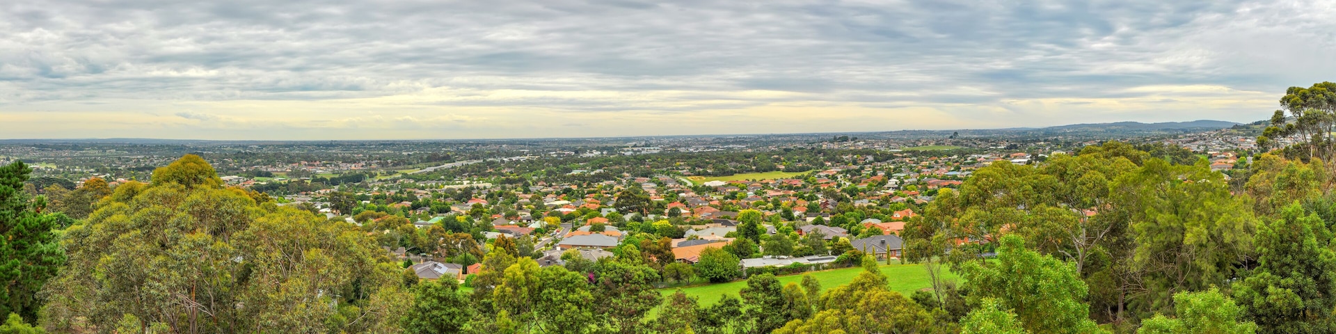 Une vue panoramique d’une ville nichée au milieu de collines verdoyantes, avec un mélange de maisons résidentielles et d’espaces ouverts.