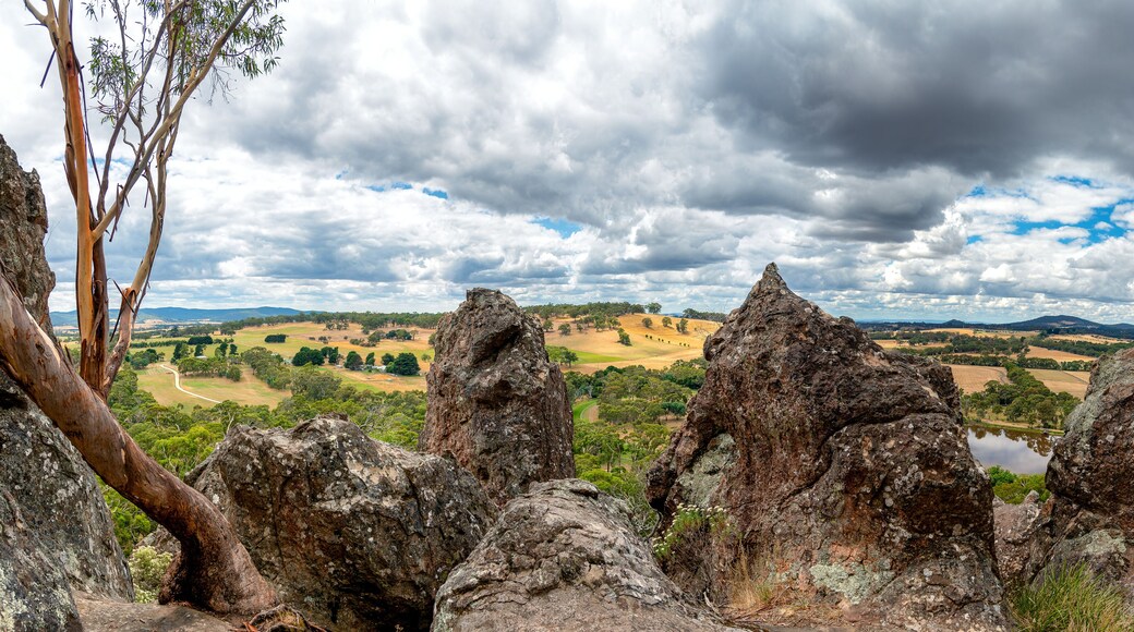A panoramic view from Hanging Rock in Victoria, Australia, with volcanic boulders in the foreground and rolling hills in the distance