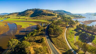 A winding road through a hilly landscape with a river and patches of waterlogged fields.