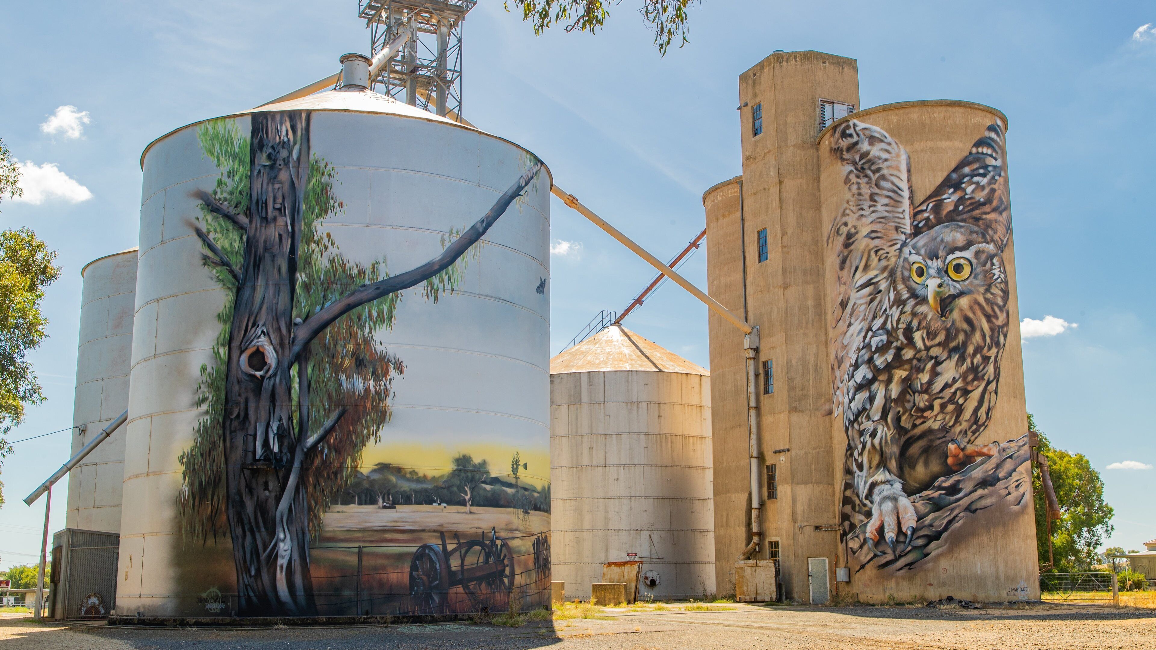 Large grain silos with detailed murals of a tree and an owl.