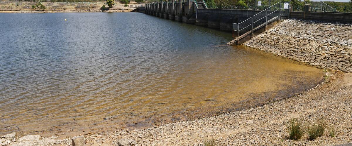 A dam with a concrete spillway and a rocky shore.