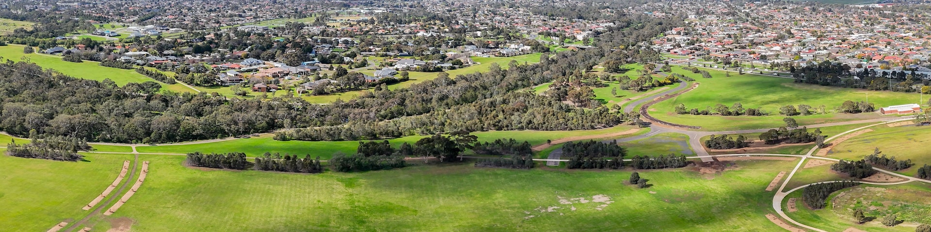 Une vue aérienne d’une ville avec des quartiers résidentiels, des champs verdoyants et un parc.